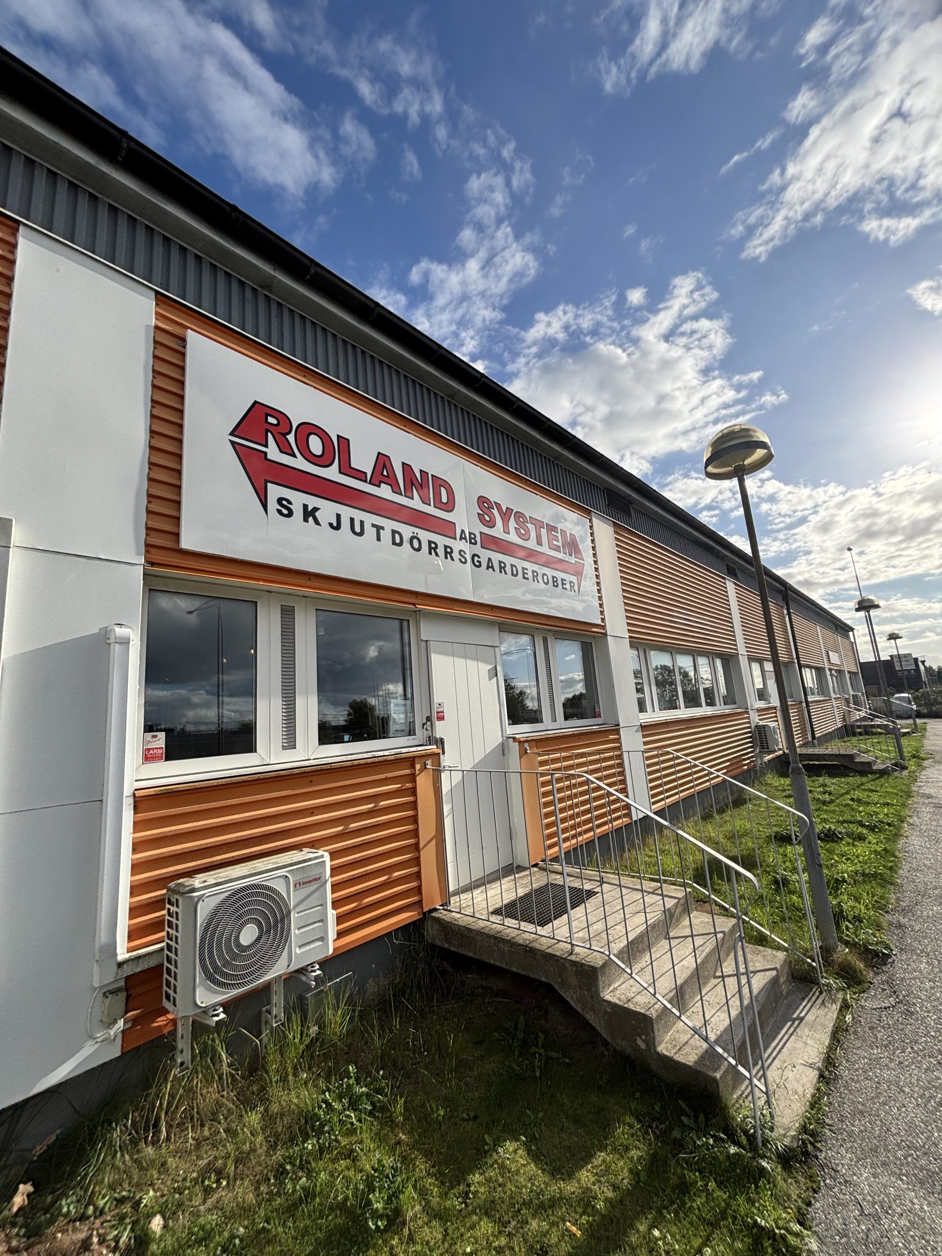 Envåningsbyggnad med orange fasad och en stor Roland System-skylt ovanför fönstren och entrén.