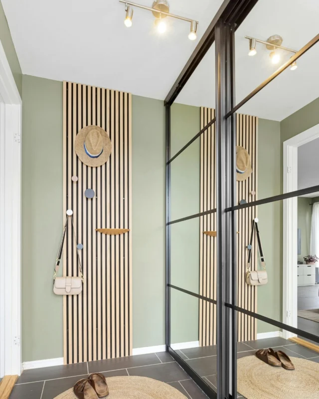 Hallway with black-framed glass sliding doors in front of a slatted wood wall with hooks