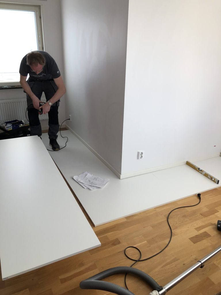 Installer assembling a white wardrobe interior in an empty room, with panels laid out on the floor.
