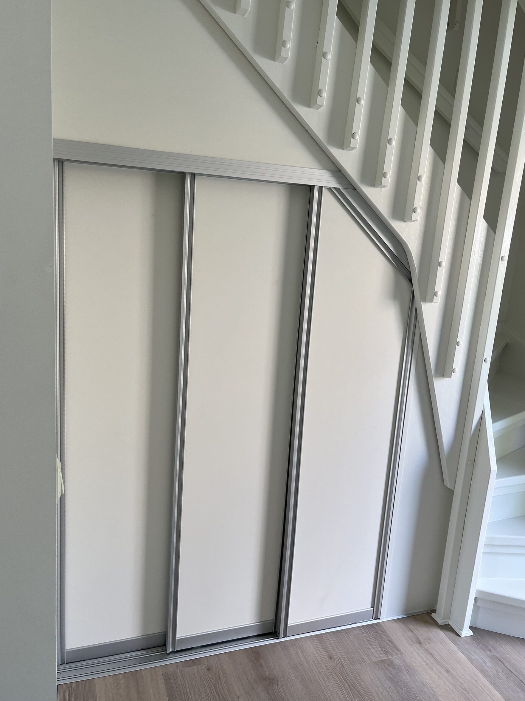 White sliding doors under a staircase, with the top of the doors following the slope of the stairs.